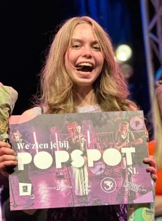 Een lachende Kikkie met de cheque met daarop "We zien je bij Popspot".